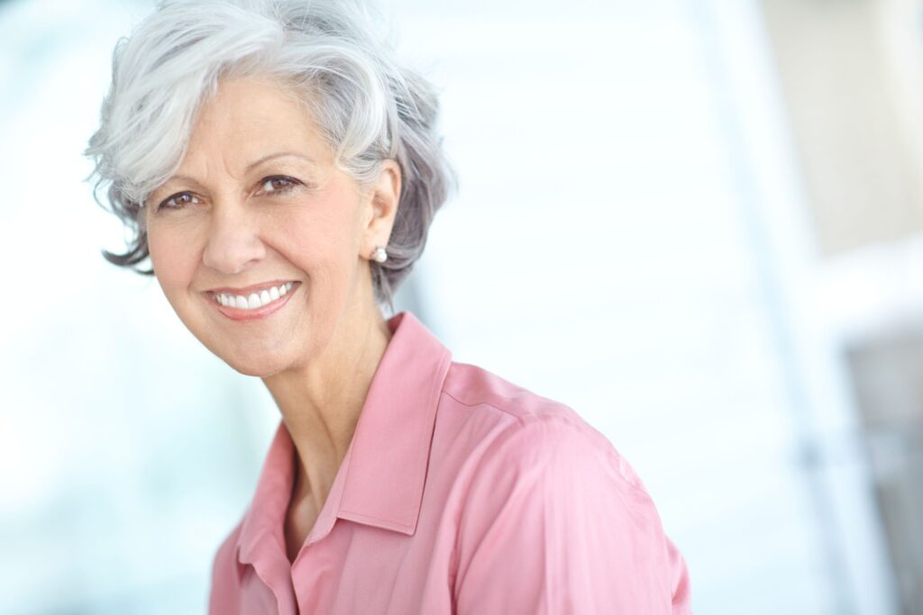 Woman with short gray hair in pink shirt smiling